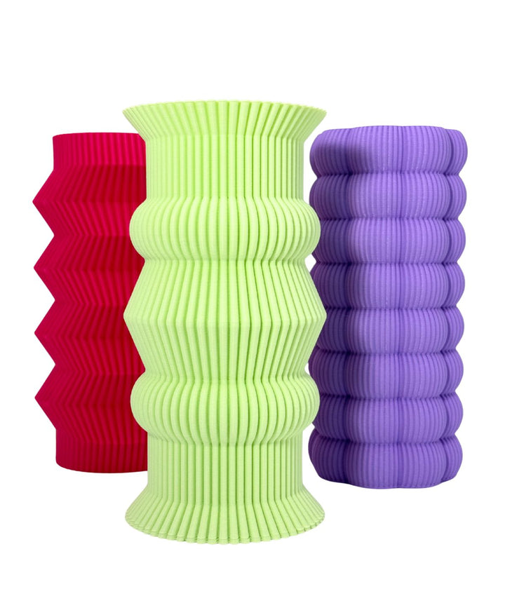 Un trio di vasi scultorei con colori vivaci e texture distinte. Da sinistra a destra: un vaso rosa brillante con motivi a zigzag, un vaso verde lime con eleganti contorni curvi, e un vaso viola chiaro con morbide sporgenze arrotondate.