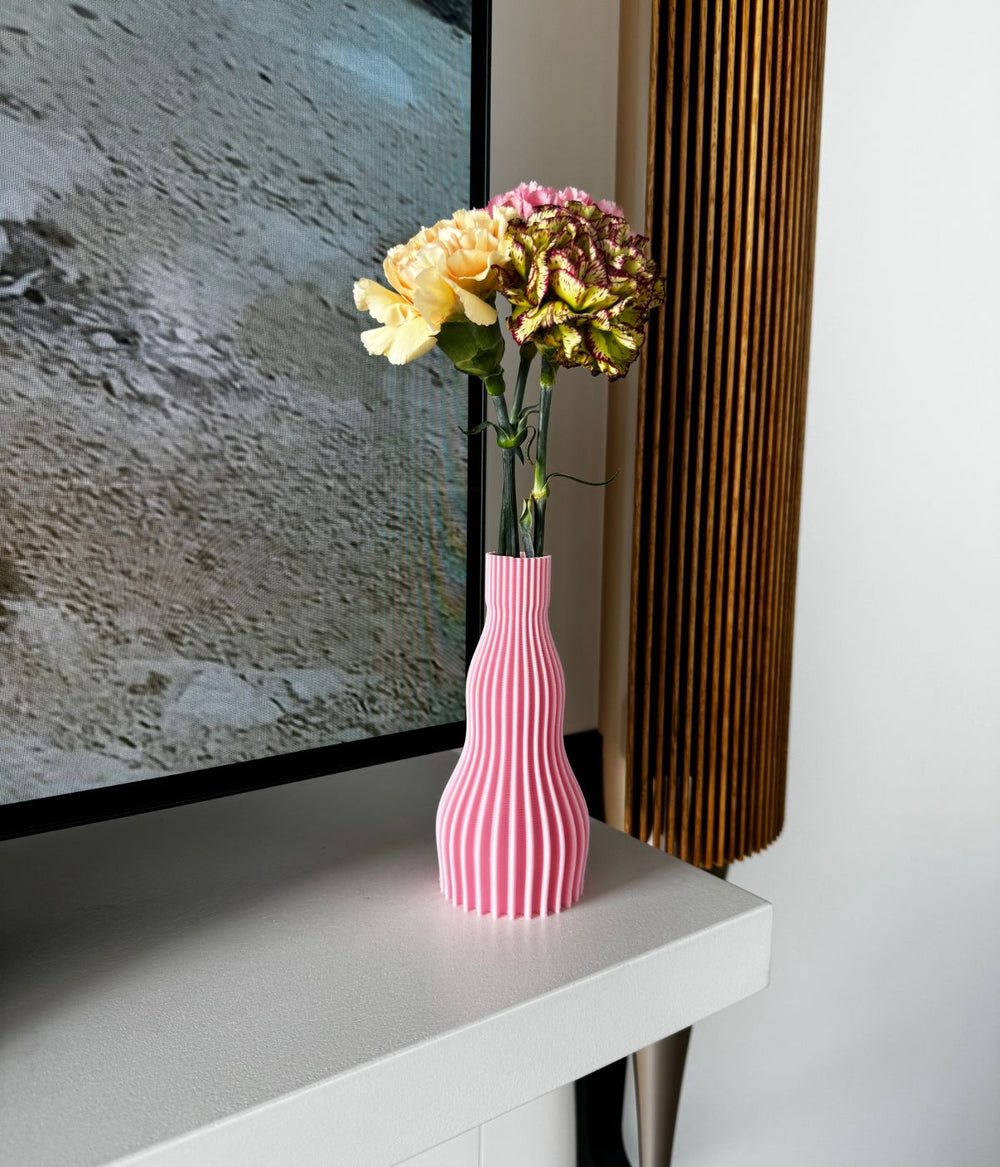 Vaso rosa di Studio Maracuja con fiori colorati, posizionato su una mensola vicino a una TV.