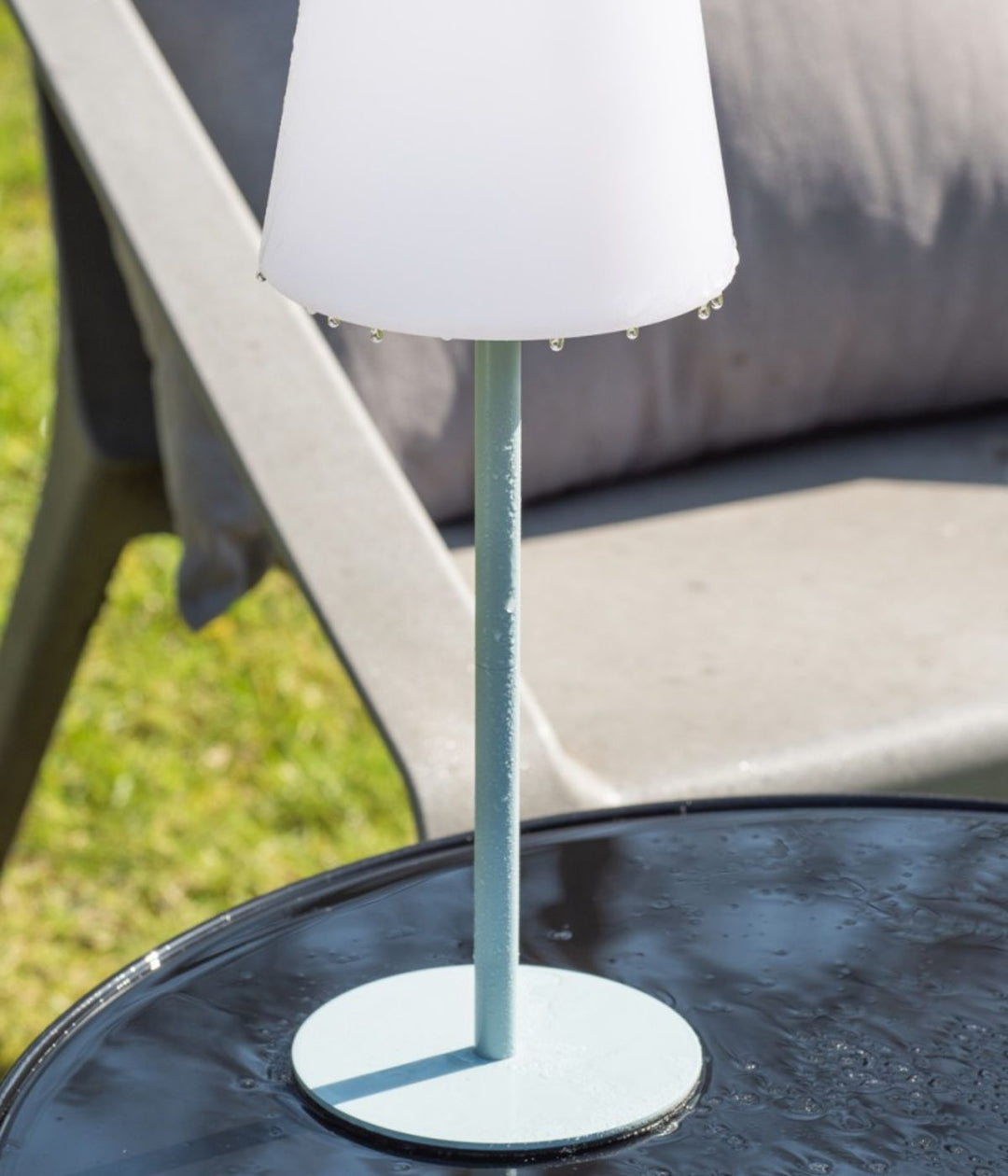 Lampada da tavolo Outdoors azzurra su tavolo da giardino bagnato dalla pioggia.