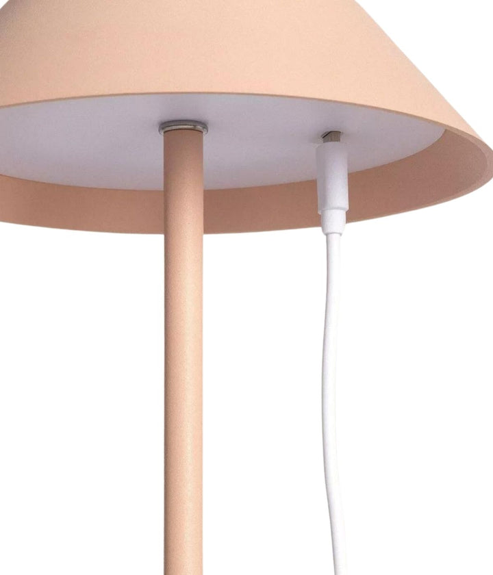 Primo piano di una Lampada da Tavolo Led Senza Fili in rosa chiaro di Keep The Design Up con un supporto sottile abbinato. un cavo di alimentazione bianco è collegato al lato della lampada.