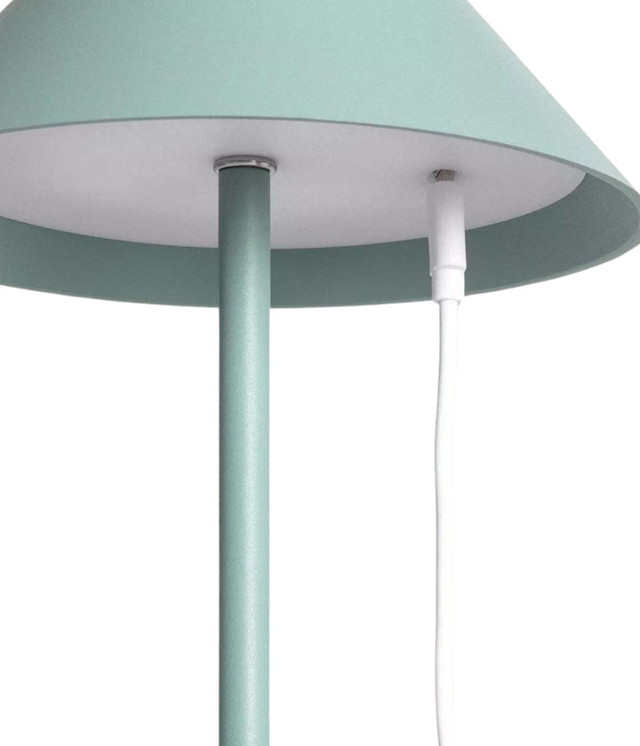 Primo piano di una lampada da tavolo Led Senza Fili Keep The Design Up in verde pastello dal design elegante, con focus sul paralume e su parte del suo supporto, con un cavo di alimentazione bianco visibile.