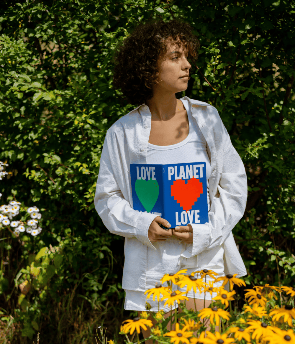 Donna con in mano il notebook aperto con scritta planet love cuore verde e rosso. Sfondo giardino.