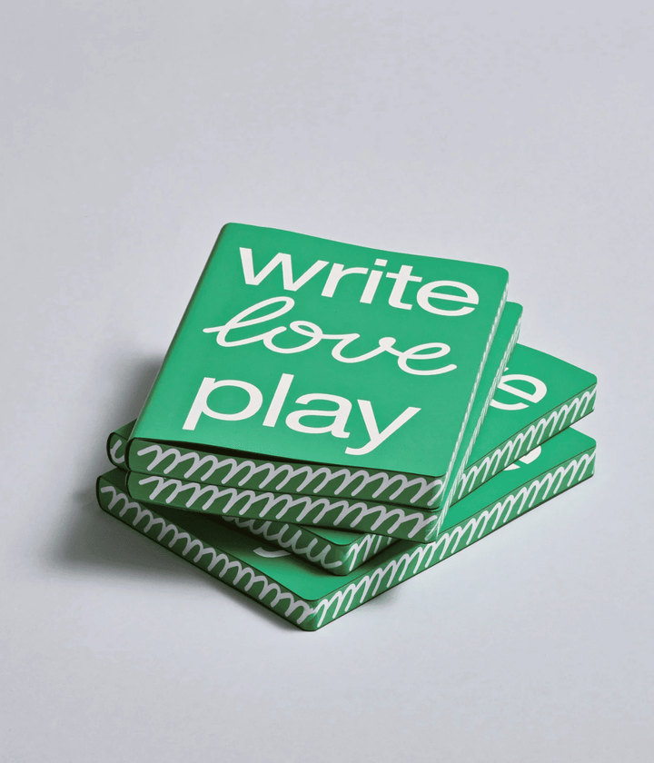 Pila di Notebook verde con scritta write love play e bordo decorato bianco. Sfondo bianco.