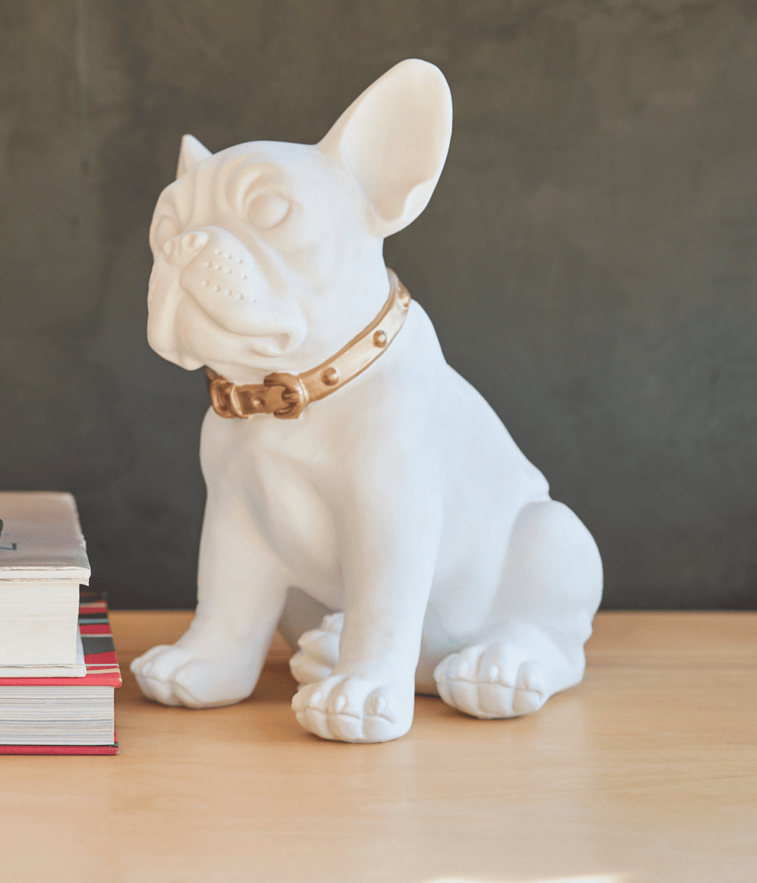 Bulldog francese bianco con guinzaglio in oro su tavolino vicino ai libri.